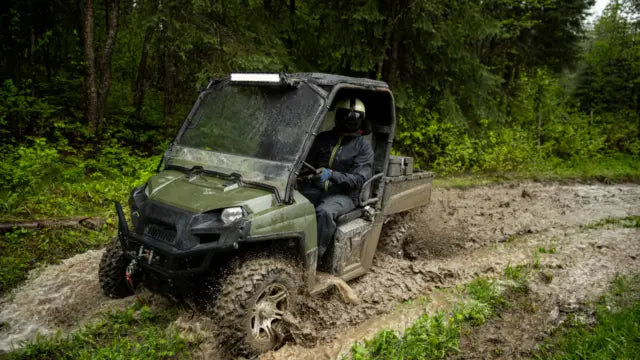 Man in helmet driving a UTV through a puddle.