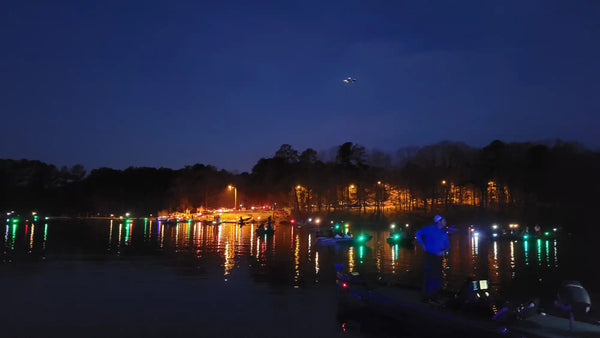 Colorful lights reflecting off a lake at night with boats along the shoreline.