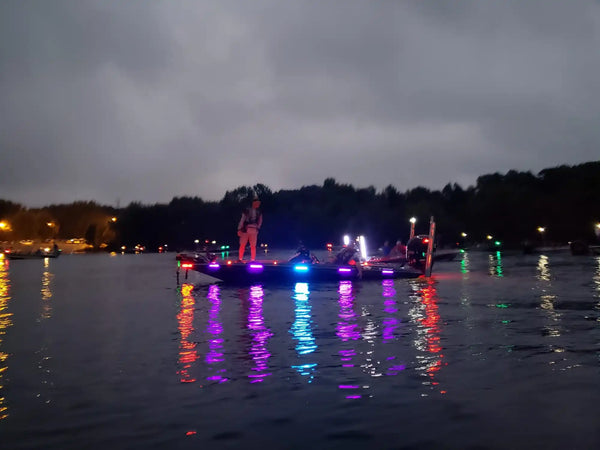 Illuminated boat decorated with colorful lights reflecting on dark water.